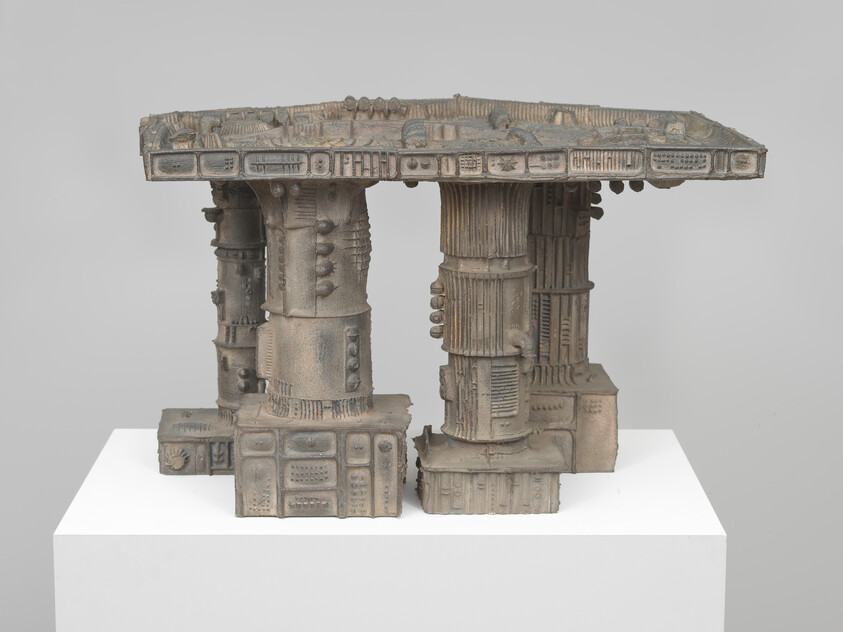 A ceramic sculptural table with three textured industrial-style pillars displayed on a white plinth.