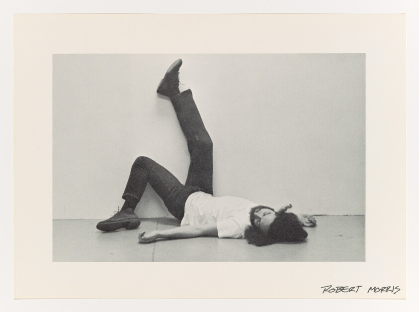 A man lies on the floor with one leg raised and resting against a blank wall.