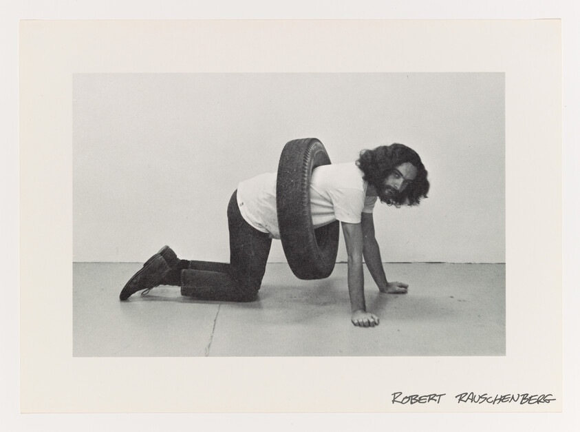 A man kneels on hands and knees with a tire looped around his torso.