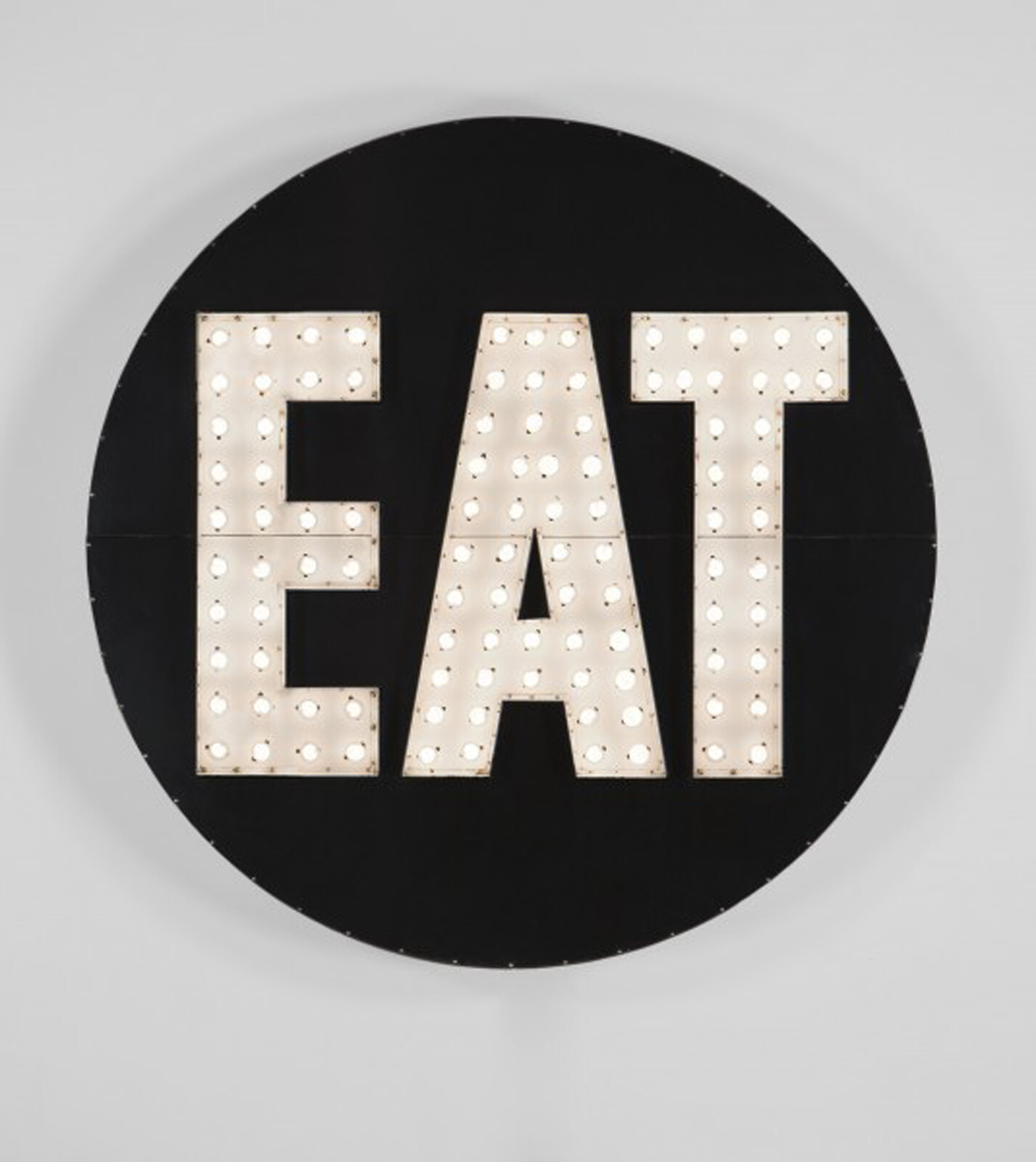 Large round black sign with illuminated marquee letters spelling EAT in bright bulbs.