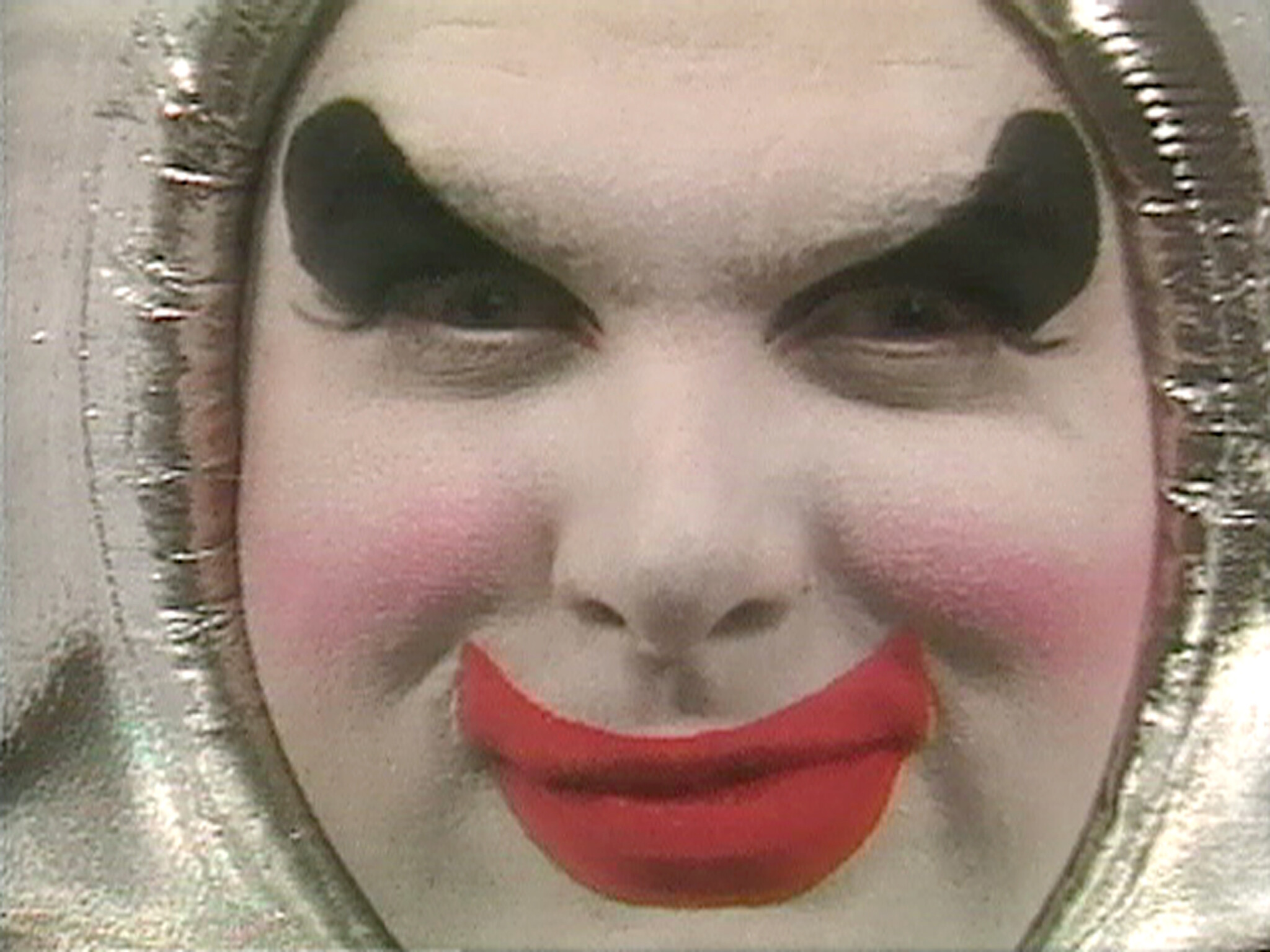 Close-up of a face with white clown makeup, bold black eyebrows, and bright red lips.