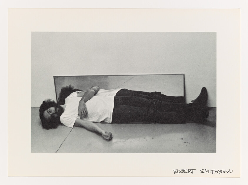 Man lying on floor with a mirror behind him reflecting his upper body and face.
