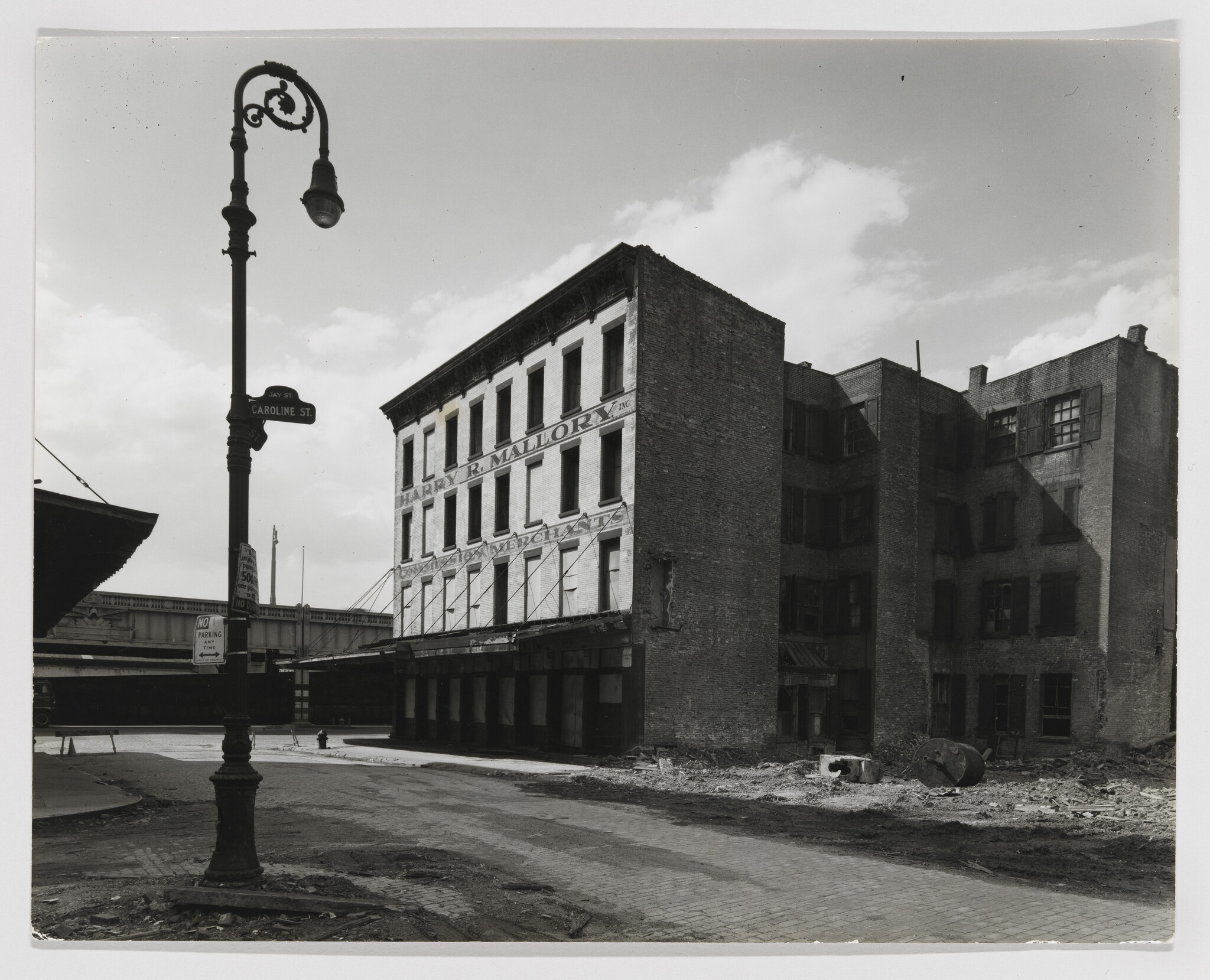 Four-story brick warehouse labeled "Harry R. Mallory" stands on a mostly empty, rubble-strewn street.