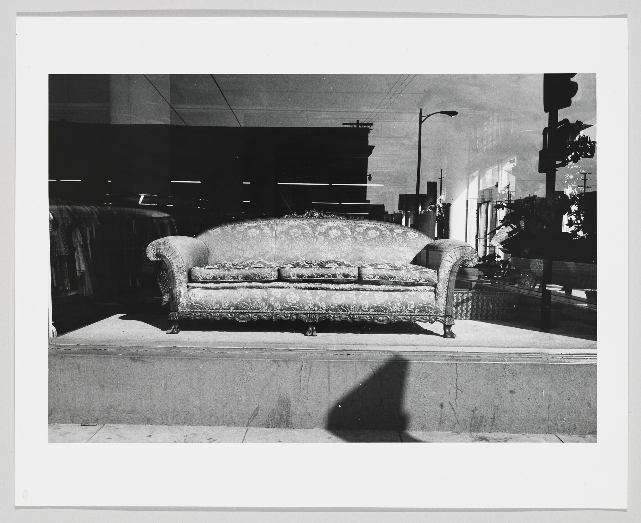 An ornate patterned sofa sits on display in a store window with street reflections visible.