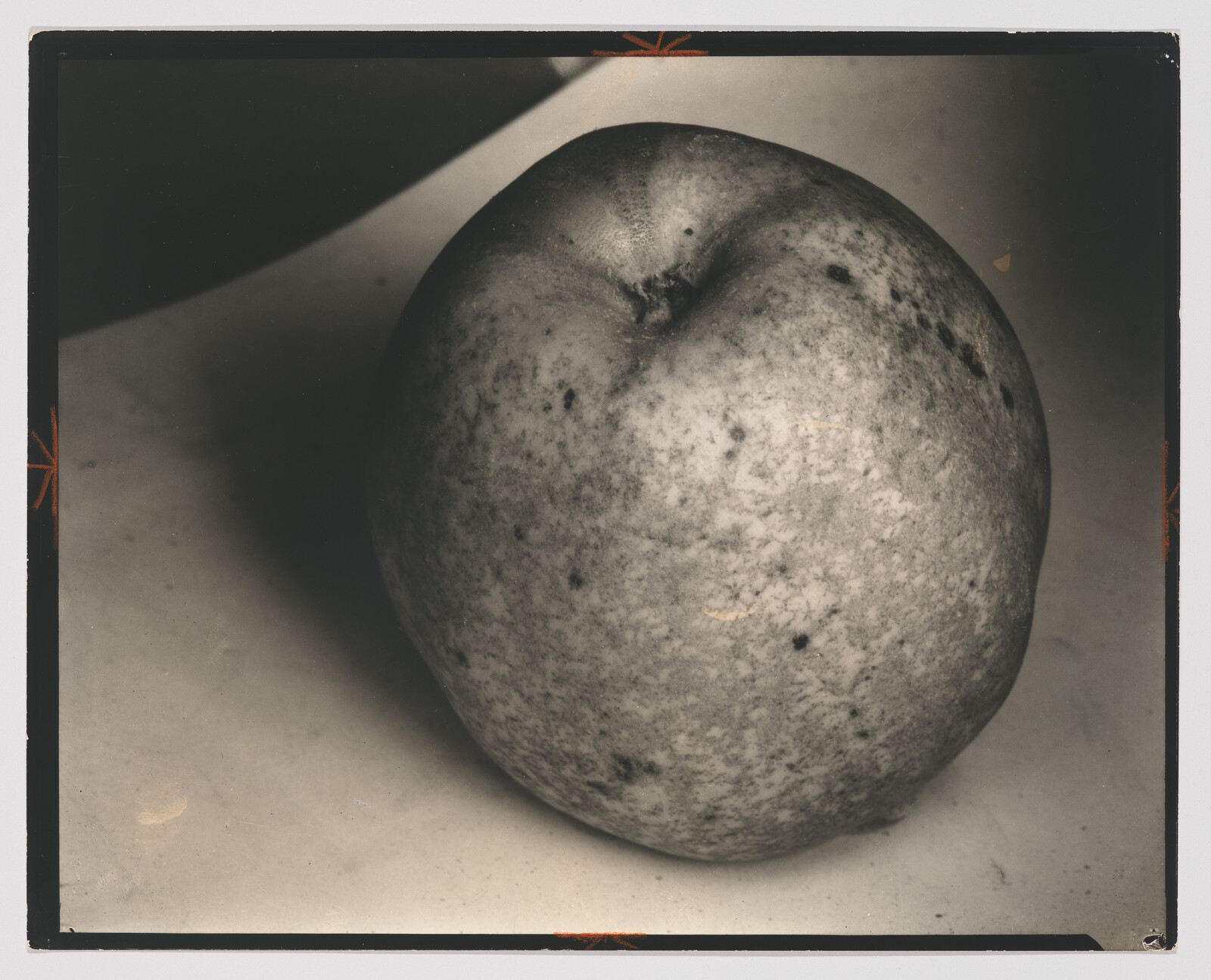 Large mottled apple sits on a plain surface with soft shadow to the left.