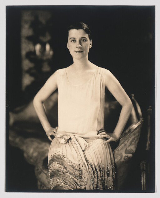 A woman stands with hands on hips wearing a sleeveless dress with a beaded skirt.