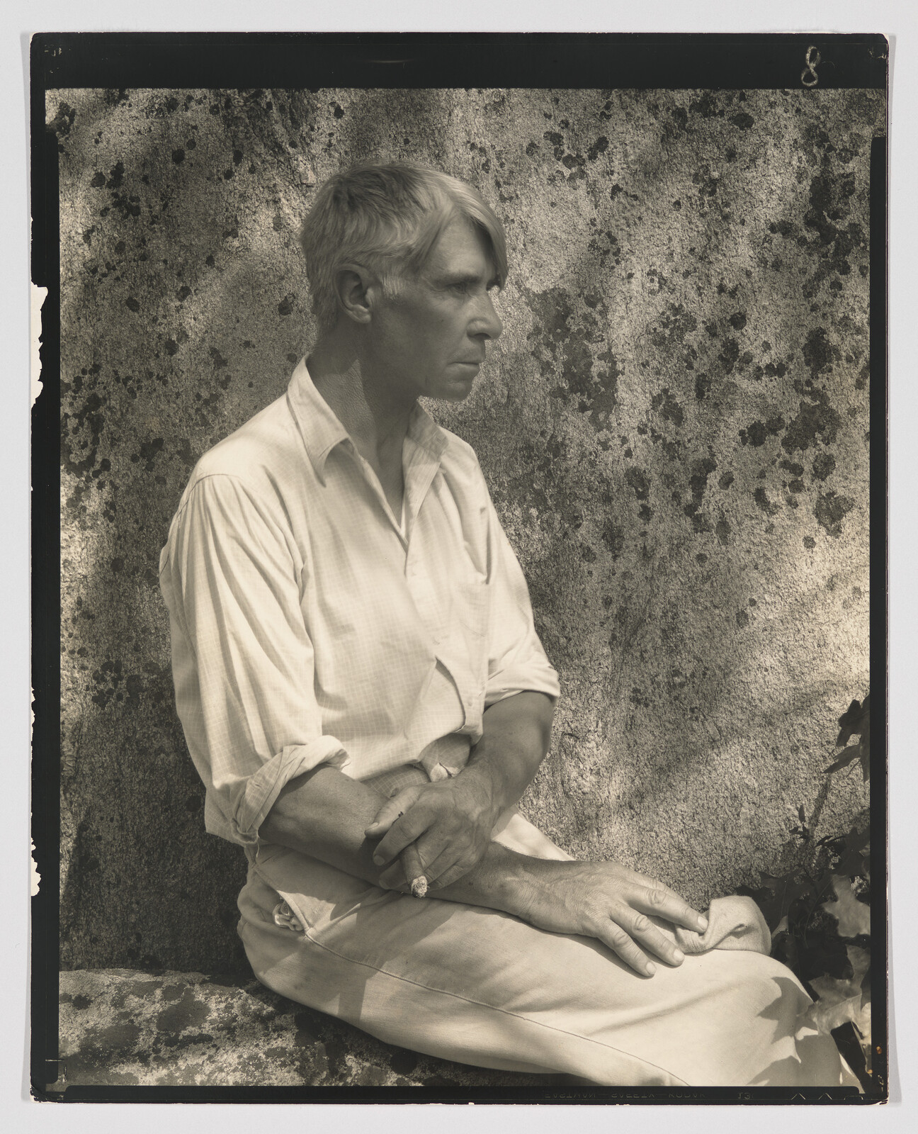 A man with folded arms sits in profile against a textured stone wall.