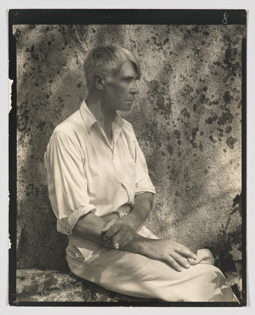 A man with folded arms sits in profile against a textured stone wall.