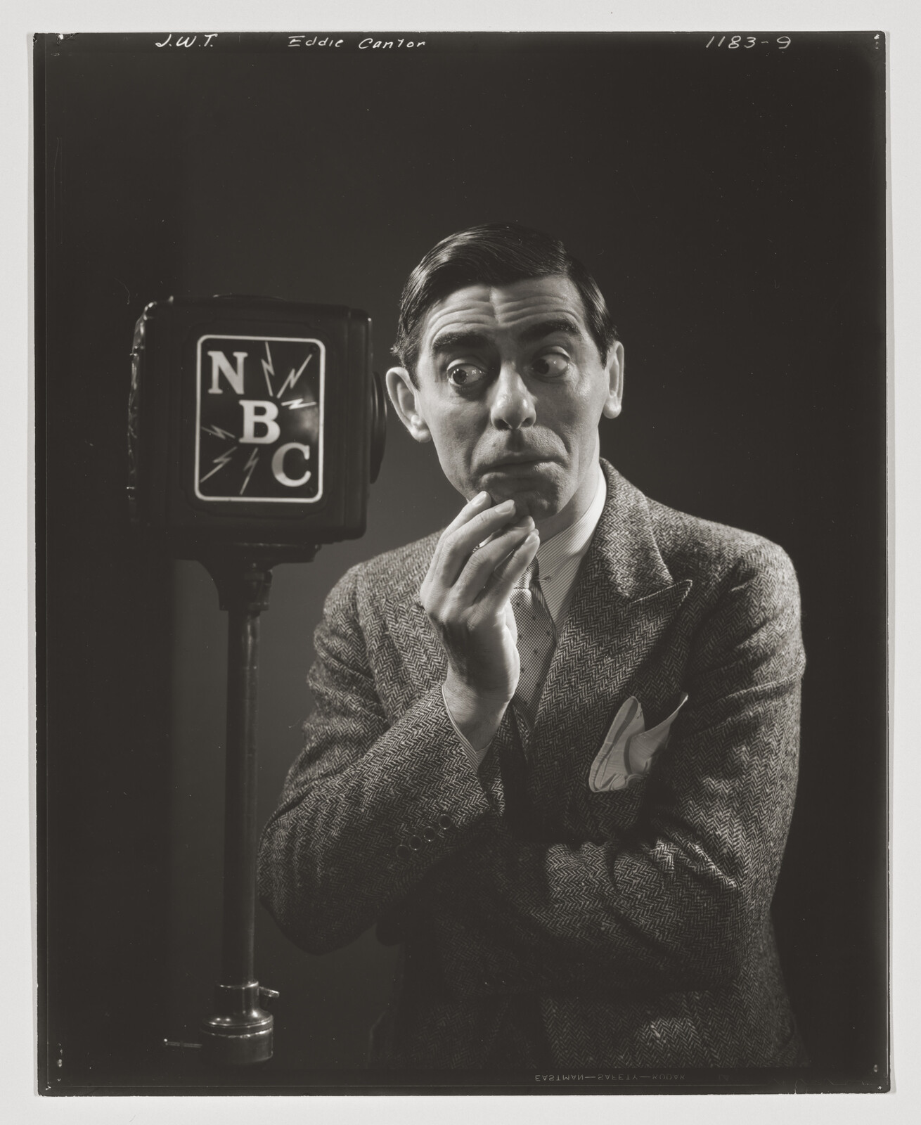 A man in a suit looks surprised while standing beside an NBC microphone.