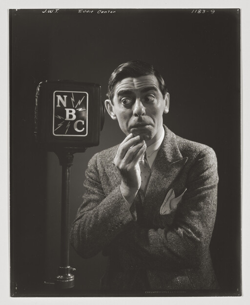 A man in a suit looks surprised while standing beside an NBC microphone.