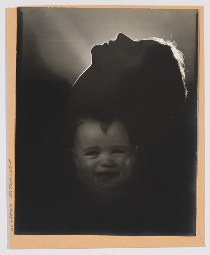 Silhouetted adult head tilted back with a softly lit, smiling baby's face appearing below.