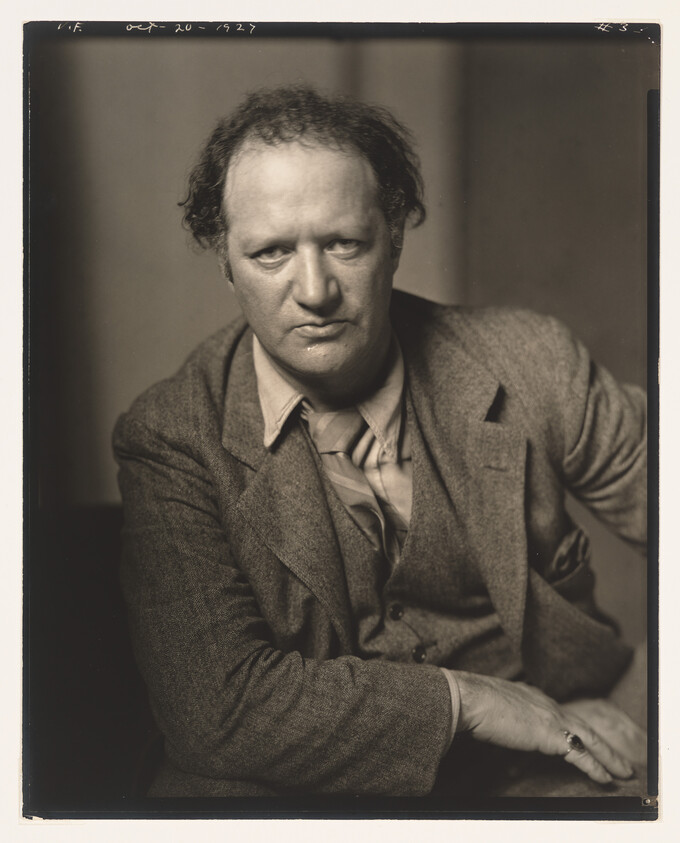 Middle-aged man in a suit leans forward with a serious expression, looking directly at the camera.