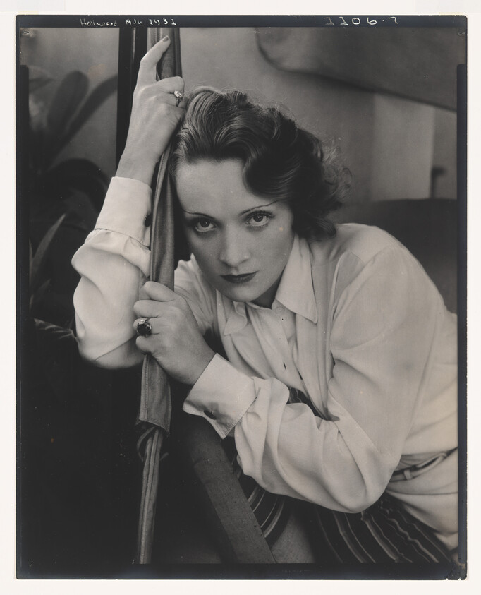 A woman with intense gaze leans forward, gripping a pole while resting her arm.