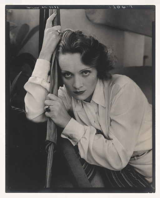 A woman with intense gaze leans forward, gripping a pole while resting her arm.