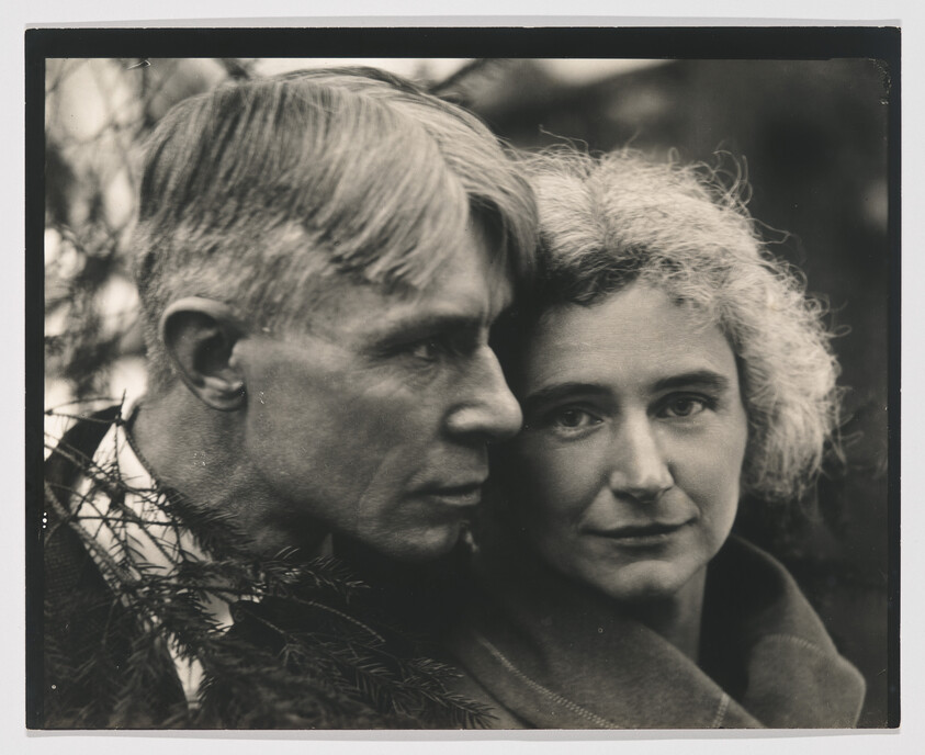 An older man and woman press their faces closely together, looking calmly toward the camera.