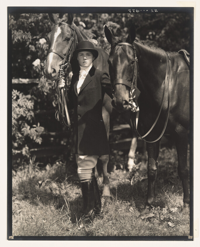 A young equestrian in riding habit stands between two saddled horses, holding their reins.