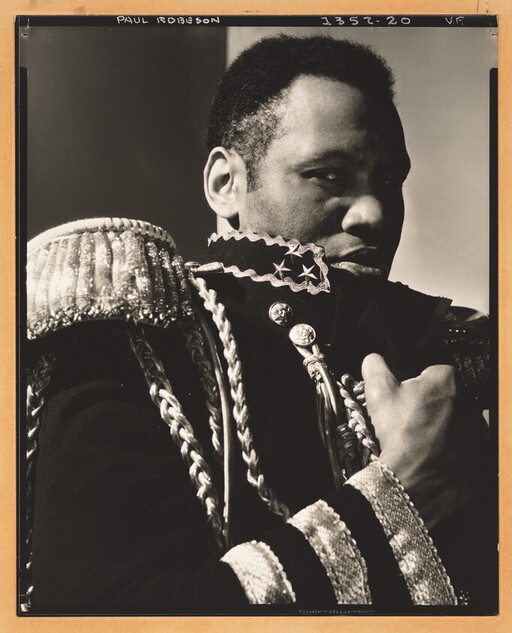 Man wearing ornate military-style jacket grasps his collar while looking to the side.