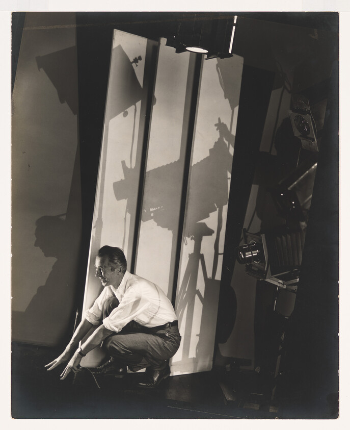 Man crouching on studio floor adjusting lighting or equipment with large shadows on the backdrop.