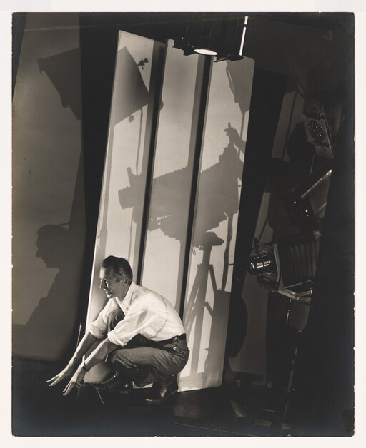 Man crouching on studio floor adjusting lighting or equipment with large shadows on the backdrop.