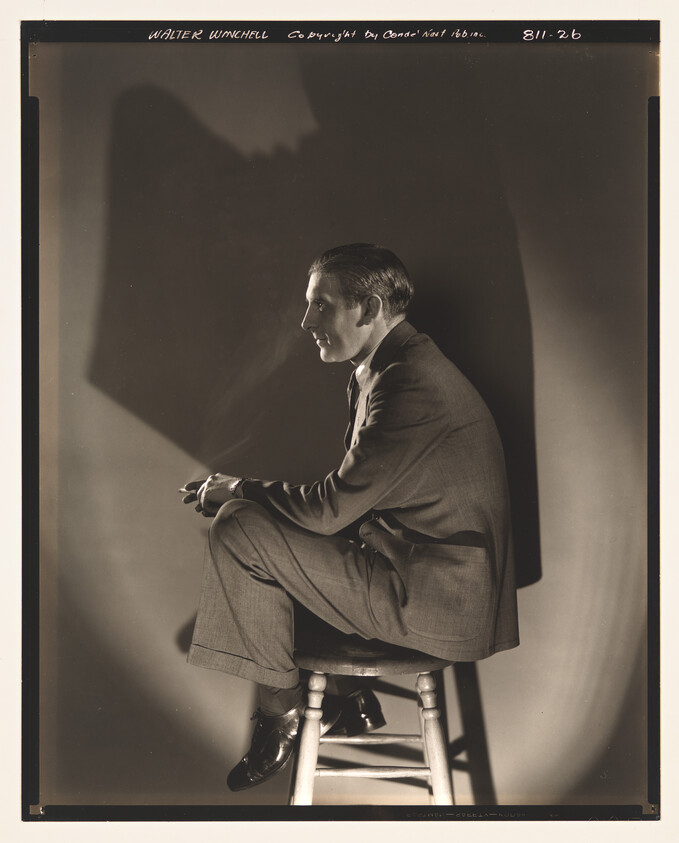 A man in a suit sits on a stool in profile, holding a cigarette and casting a shadow.