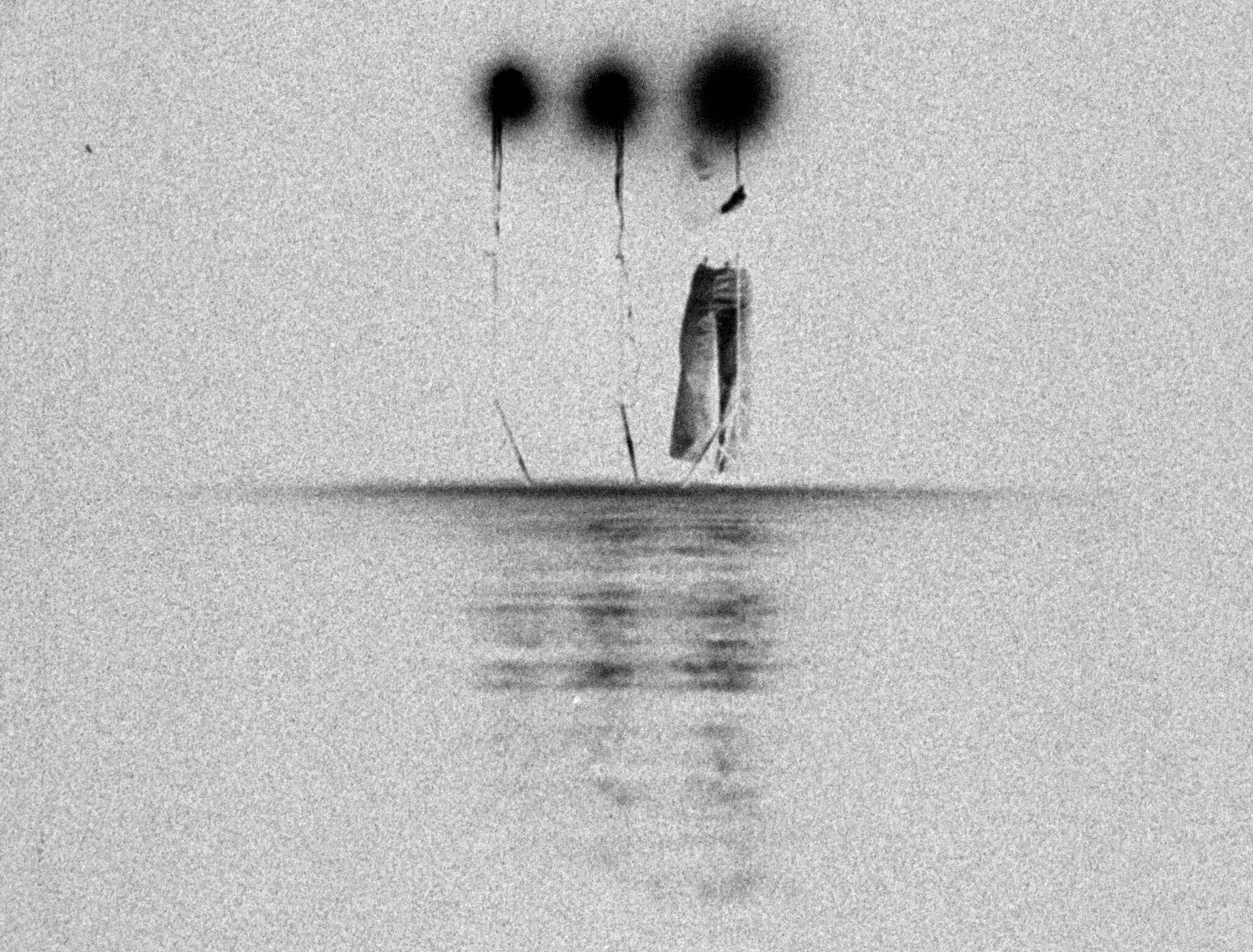 A person stands on stilts above water, with their head and hands obscured by dark spots.