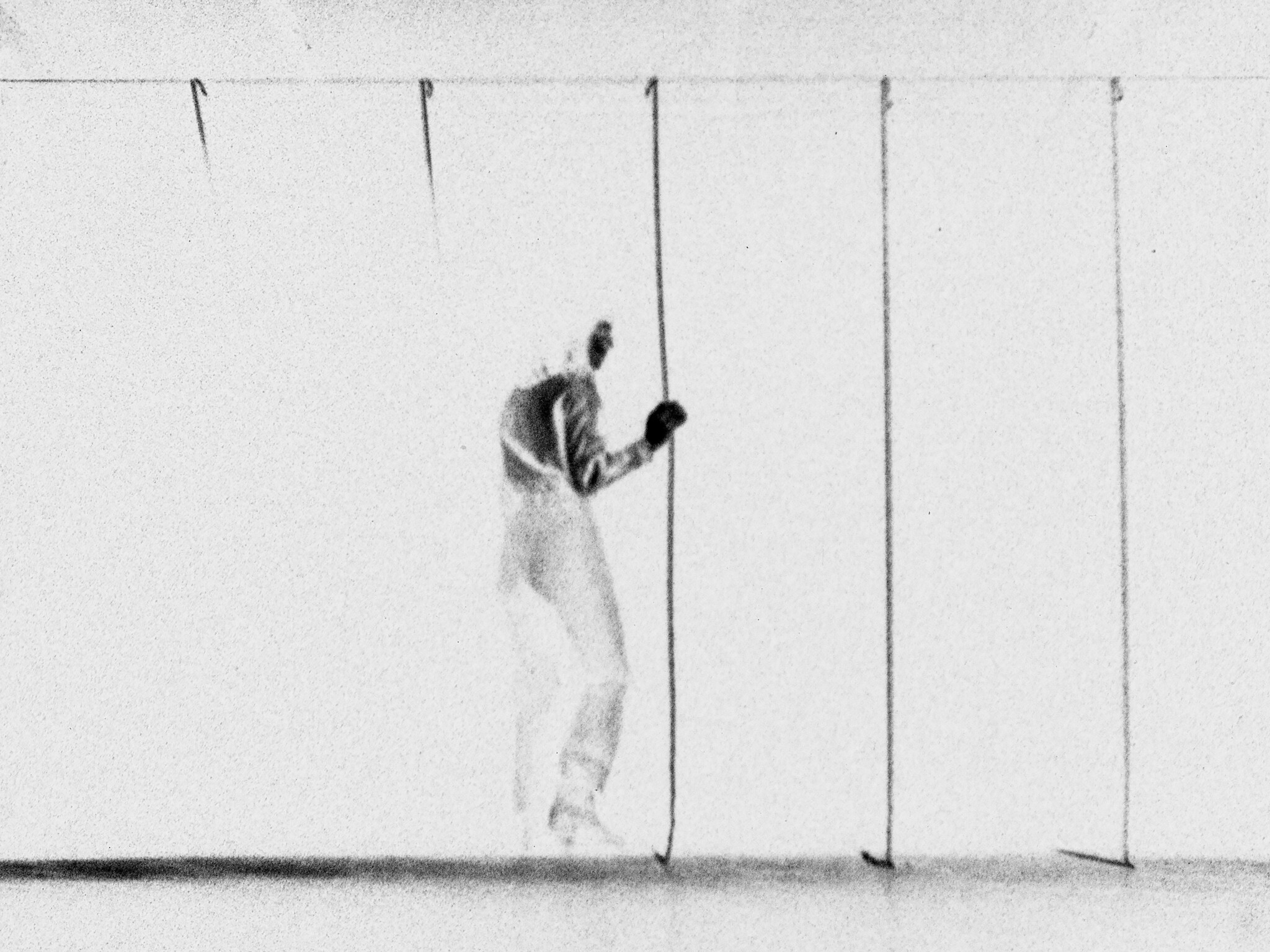 A person stands behind thin vertical lines, appearing to push or hold one of the lines with their hand.