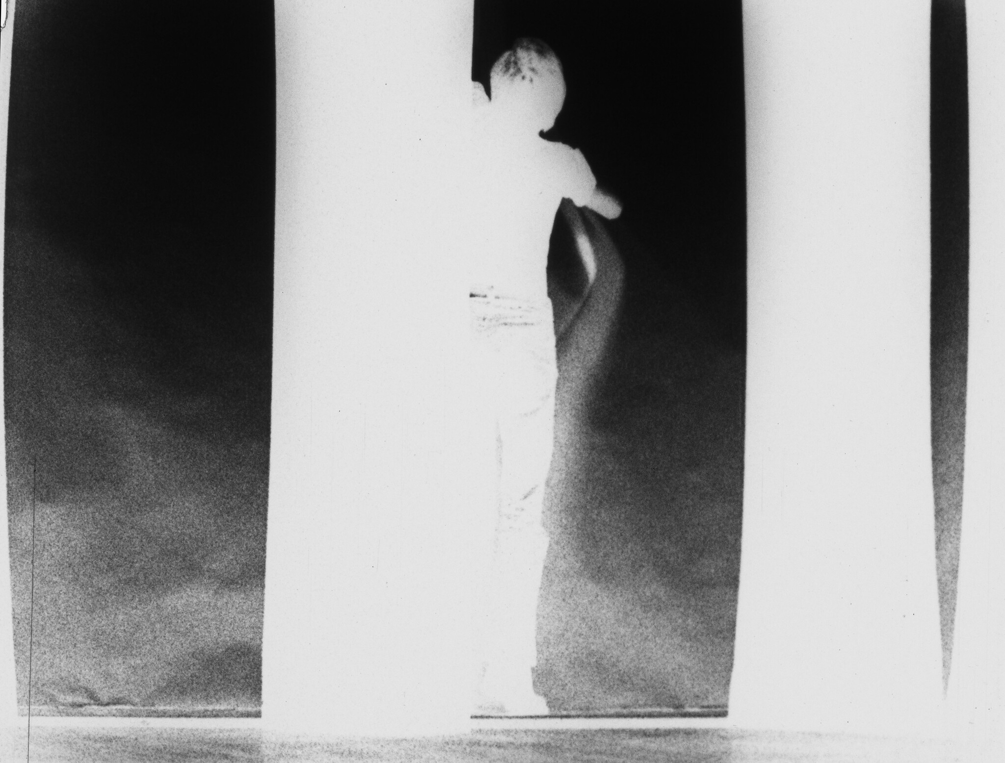 A person stands between tall vertical panels, leaning and reaching toward a dark opening.