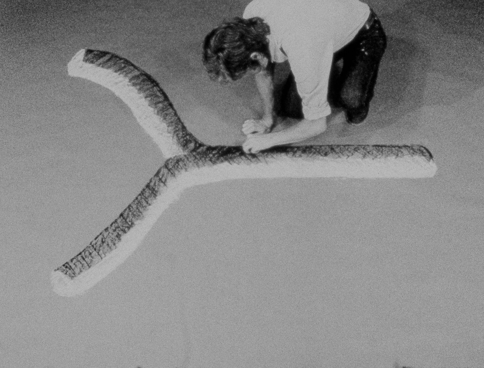 A person kneels and sketches a large three-pronged Y-shaped design on the floor.
