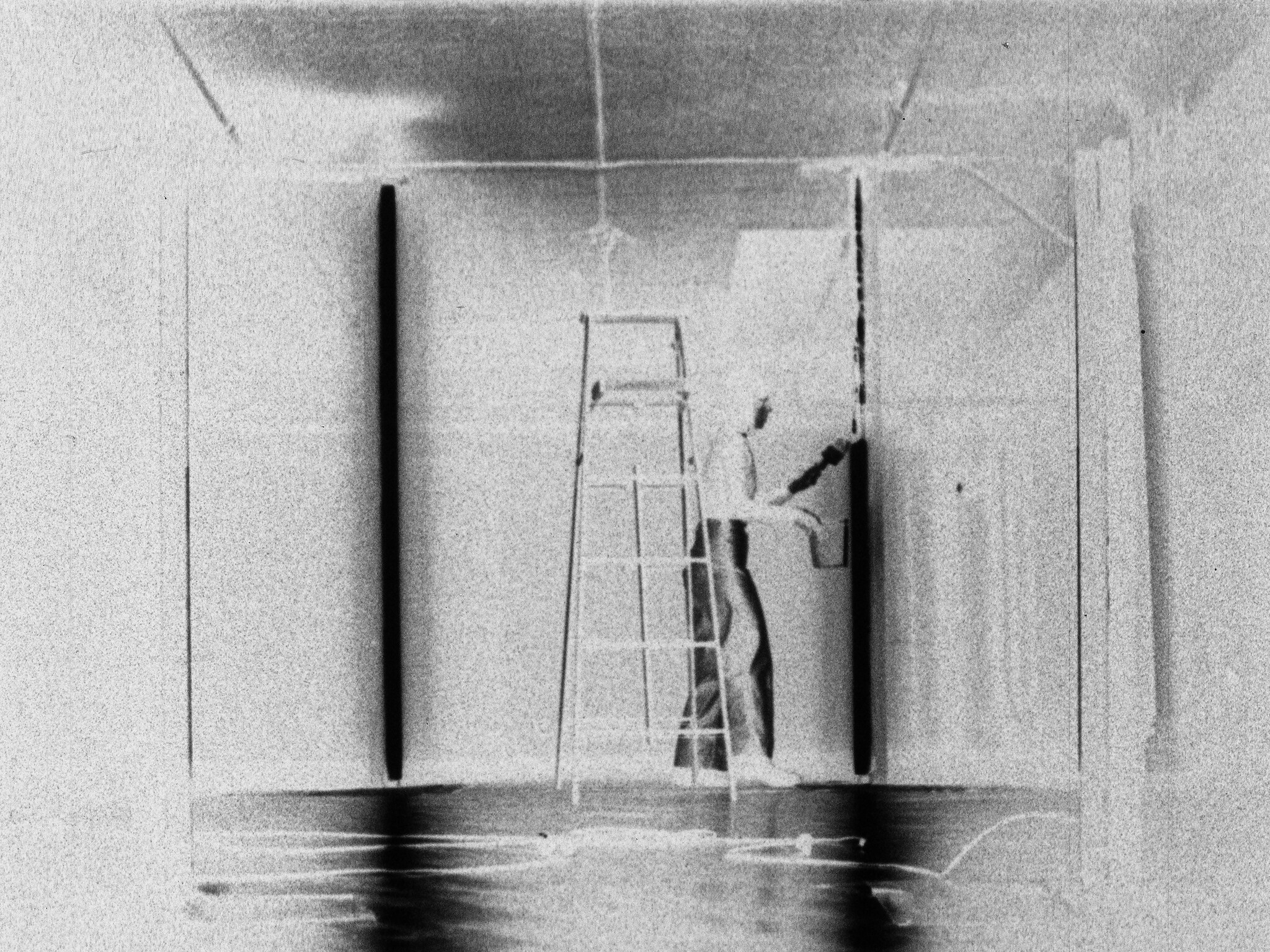 Person on a ladder painting an interior wall with a roller near the ceiling.