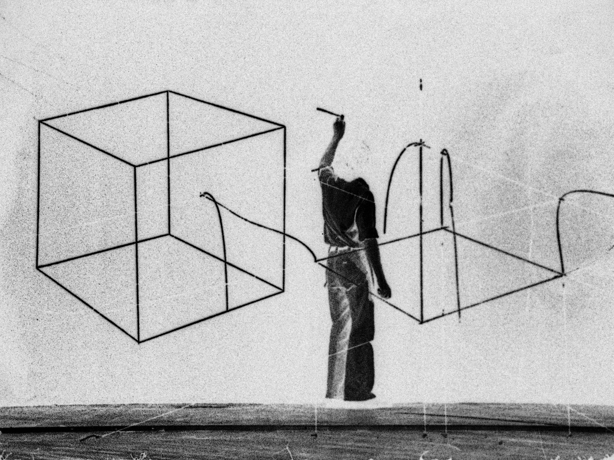 Person drawing large geometric shapes, including cubes, on a wall with a marker or pen.
