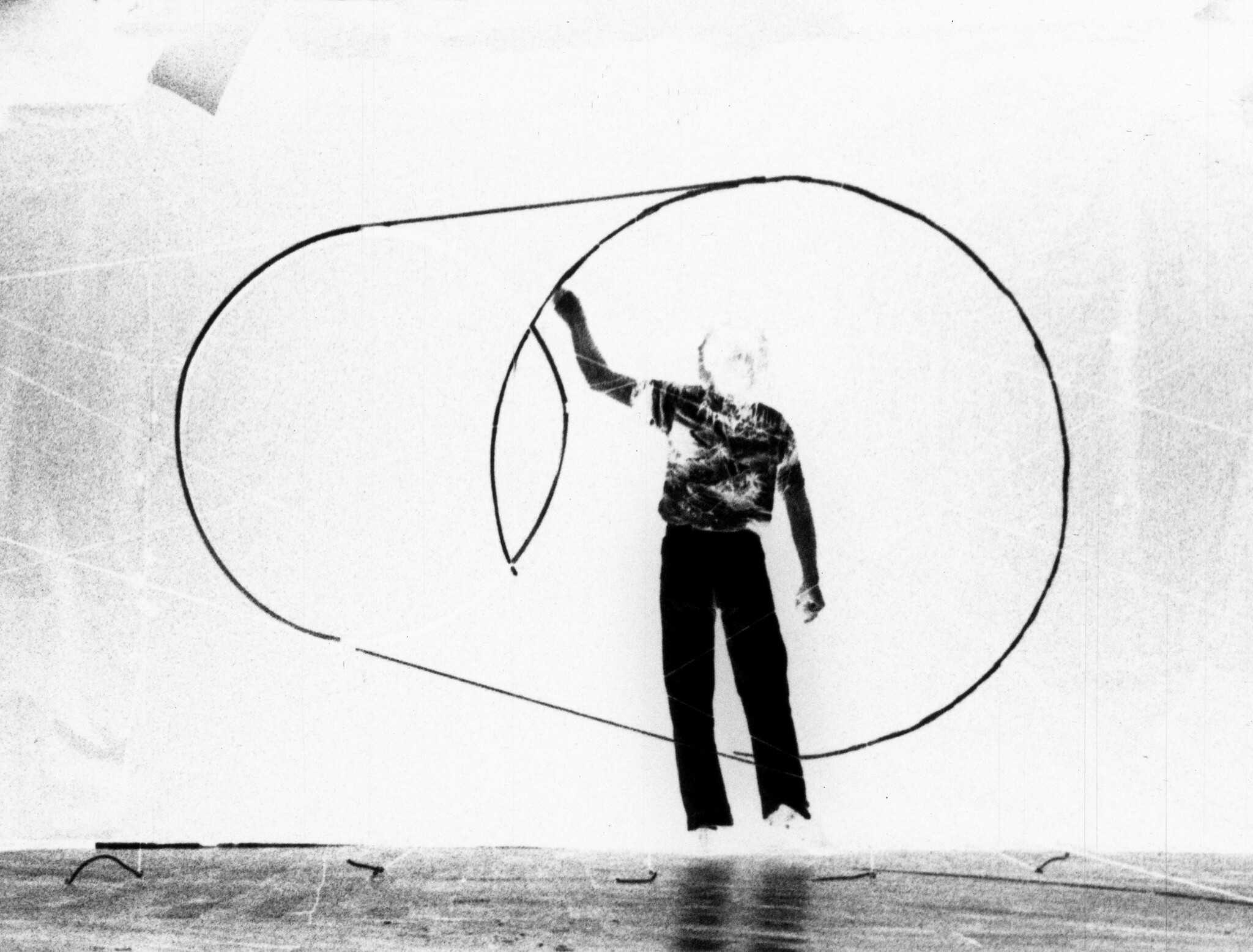 Man twirling a large looping rope creating circular shapes in open space.