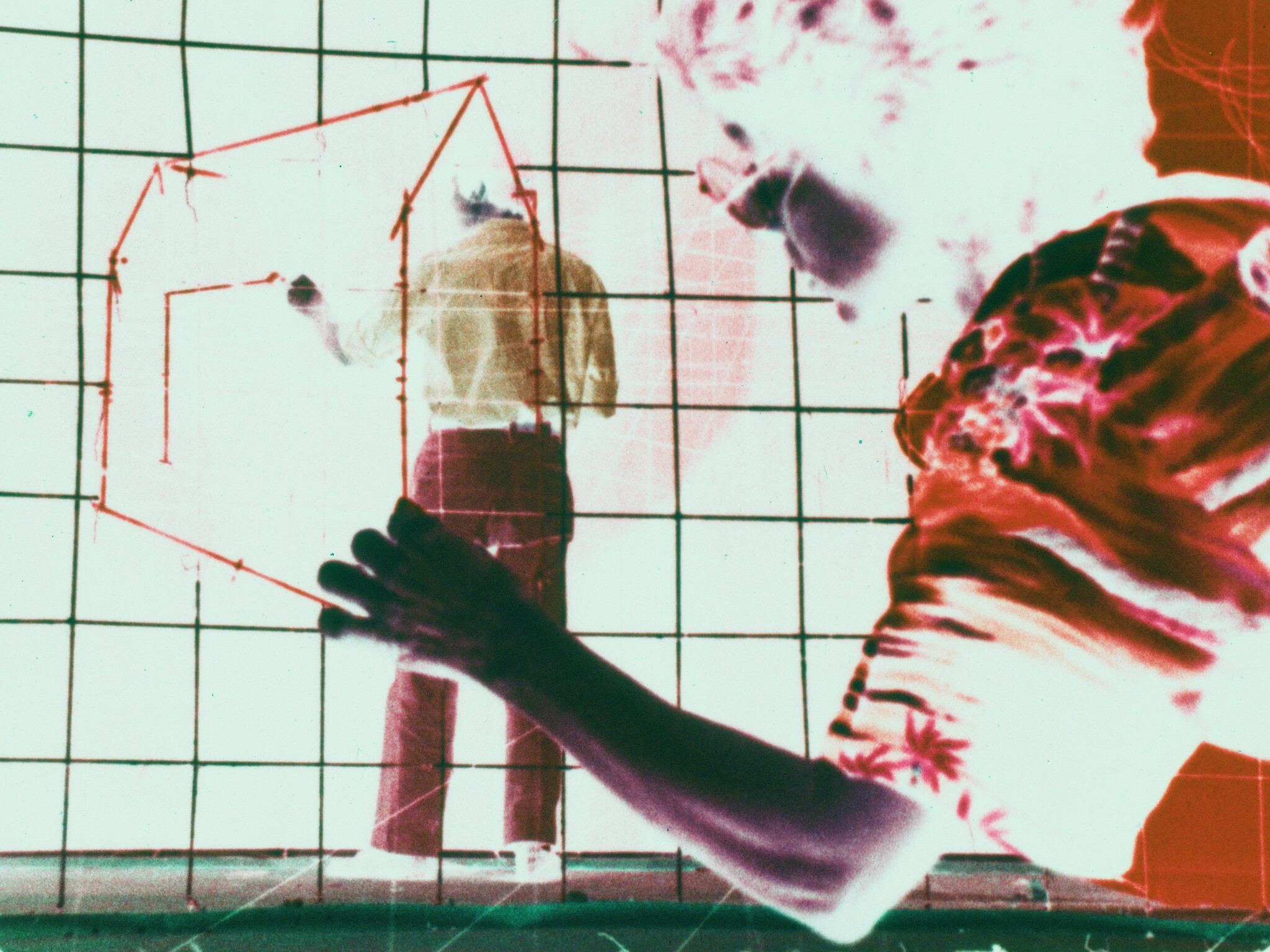 Two people interact with a large grid, drawing a red outline of a three-dimensional house shape.