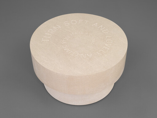 Round beige cosmetic container with embossed circular text reading "Turn soft and lovely" on the lid.