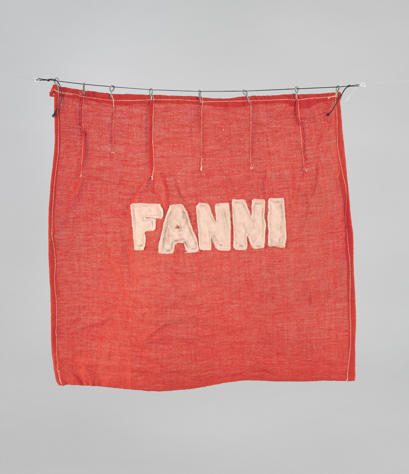 Red cloth hanging from a line with white felt letters spelling FANNI across the center.