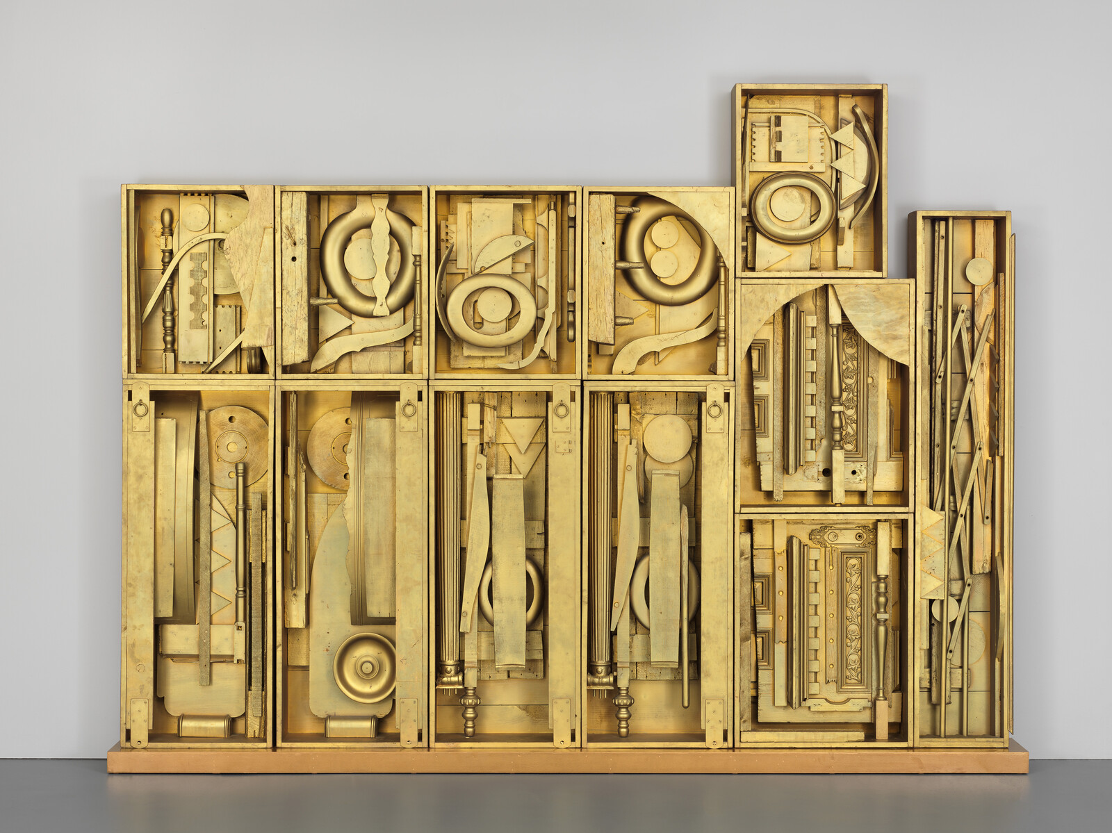 Large stacked wooden boxes filled with gold-painted architectural fragments arranged like a cabinet.