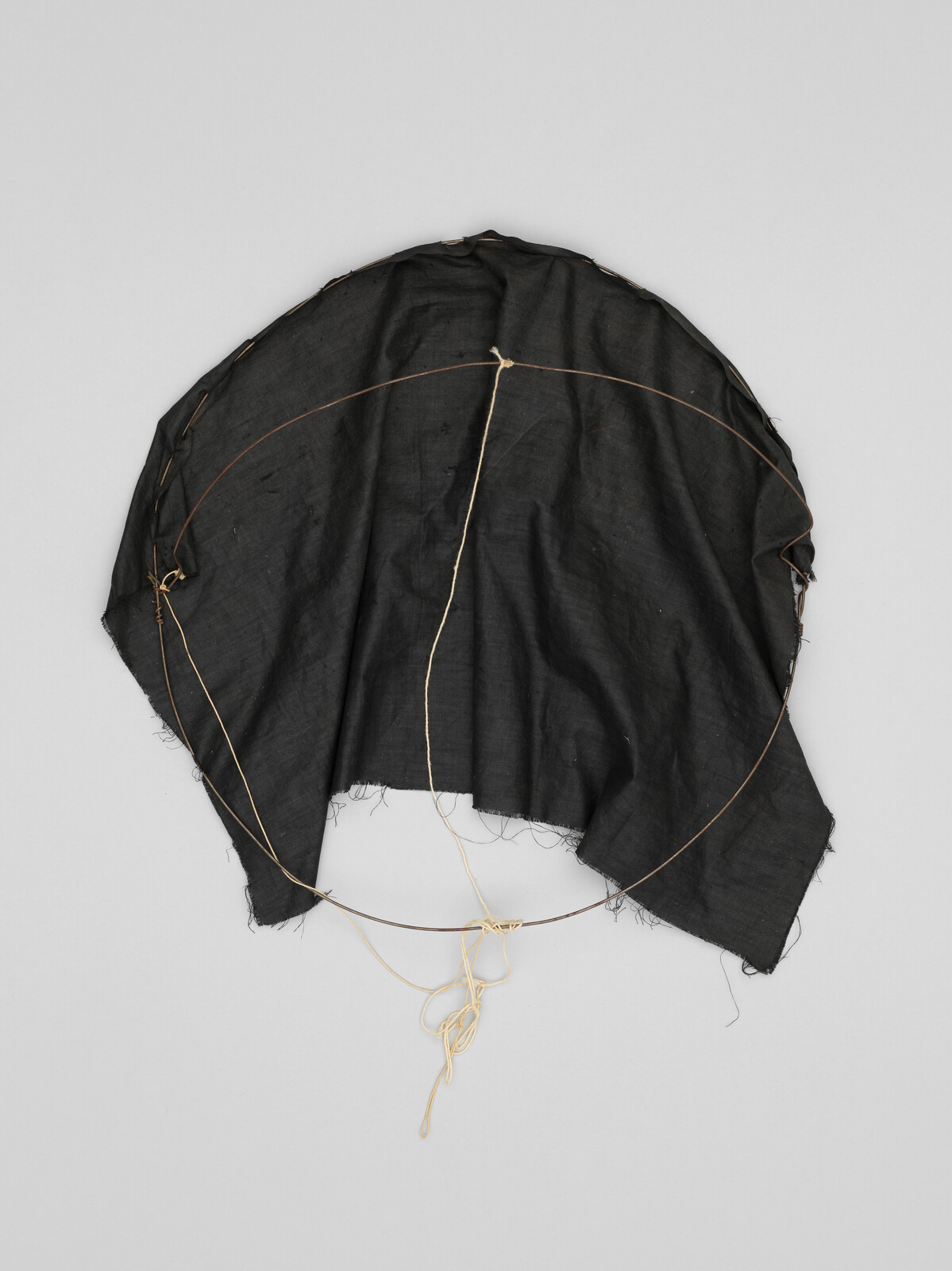 Black fabric draped over a circular wire frame with tied beige strings hanging below.