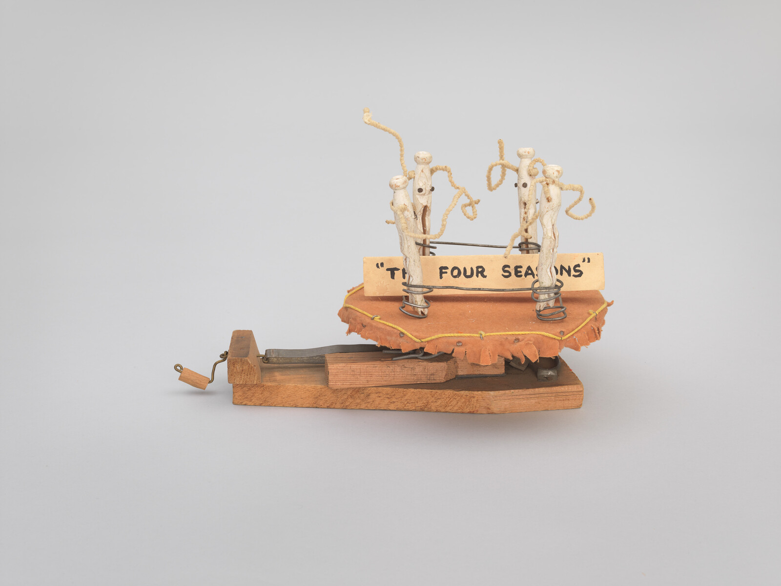 A small wooden crank toy titled "The Four Seasons" with four wire-and-wood figures on springs.