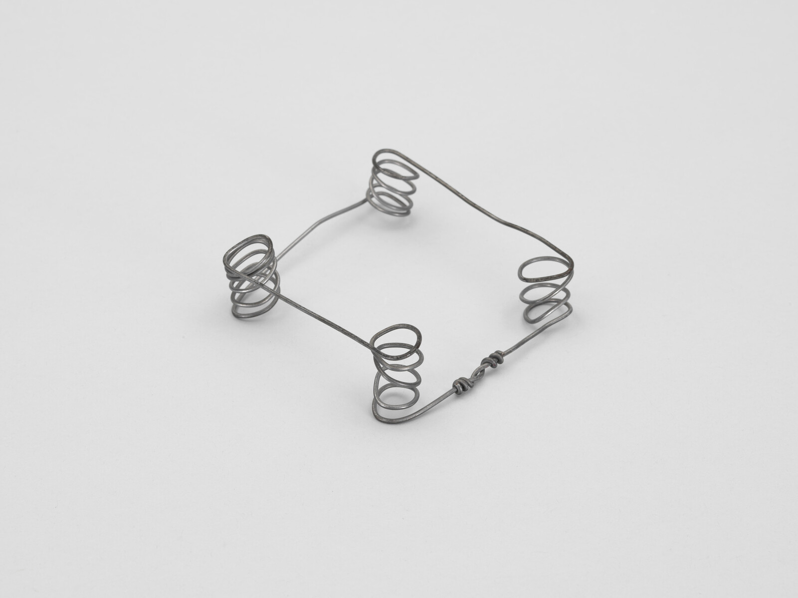 Small bent metal wire frame with four spiral coil feet arranged in a square.