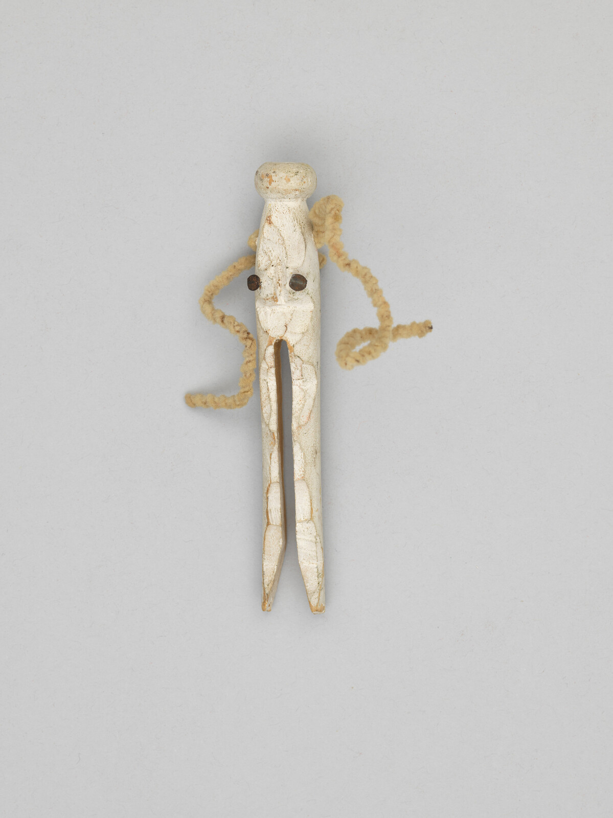 Carved white bone hairpin with two prongs and coiled fiber loops attached.