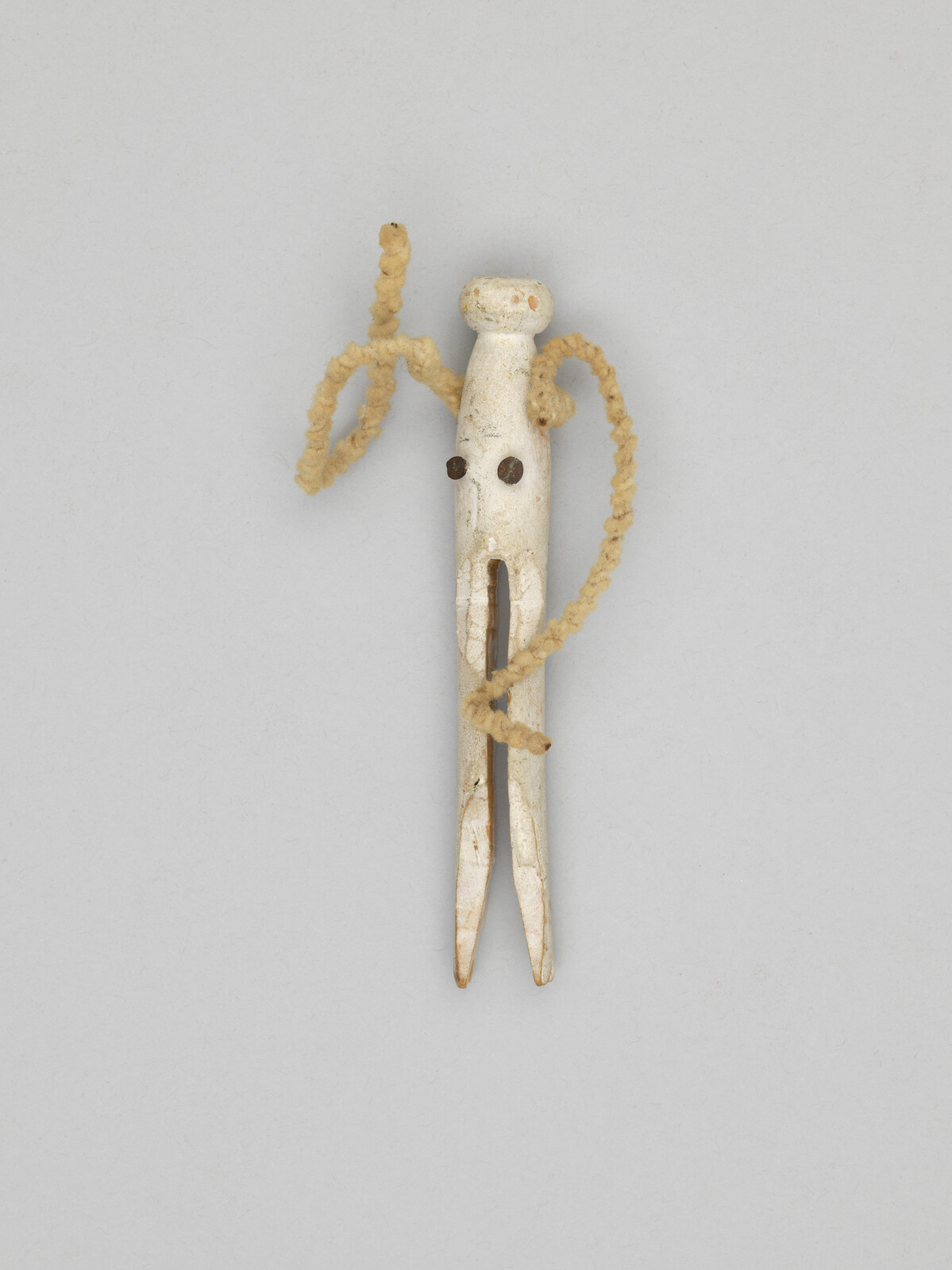 Carved bone peg with split prongs and braided cord wrapped around it like a small figure.