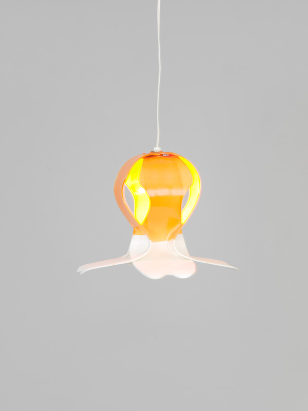 A hanging orange and white pendant lamp with petal-like curves glowing against a gray background.