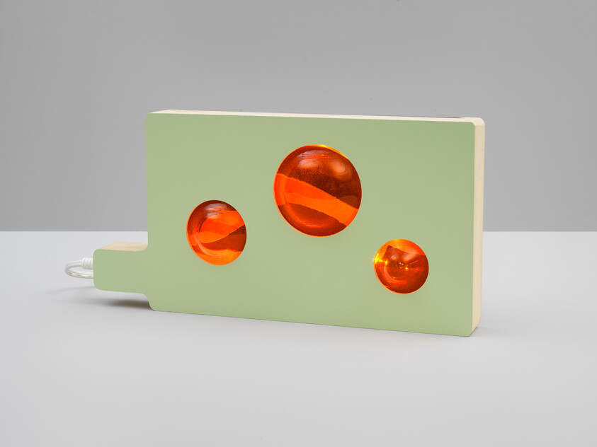 A rectangular green wooden light with three glowing orange circular windows and a power cord.