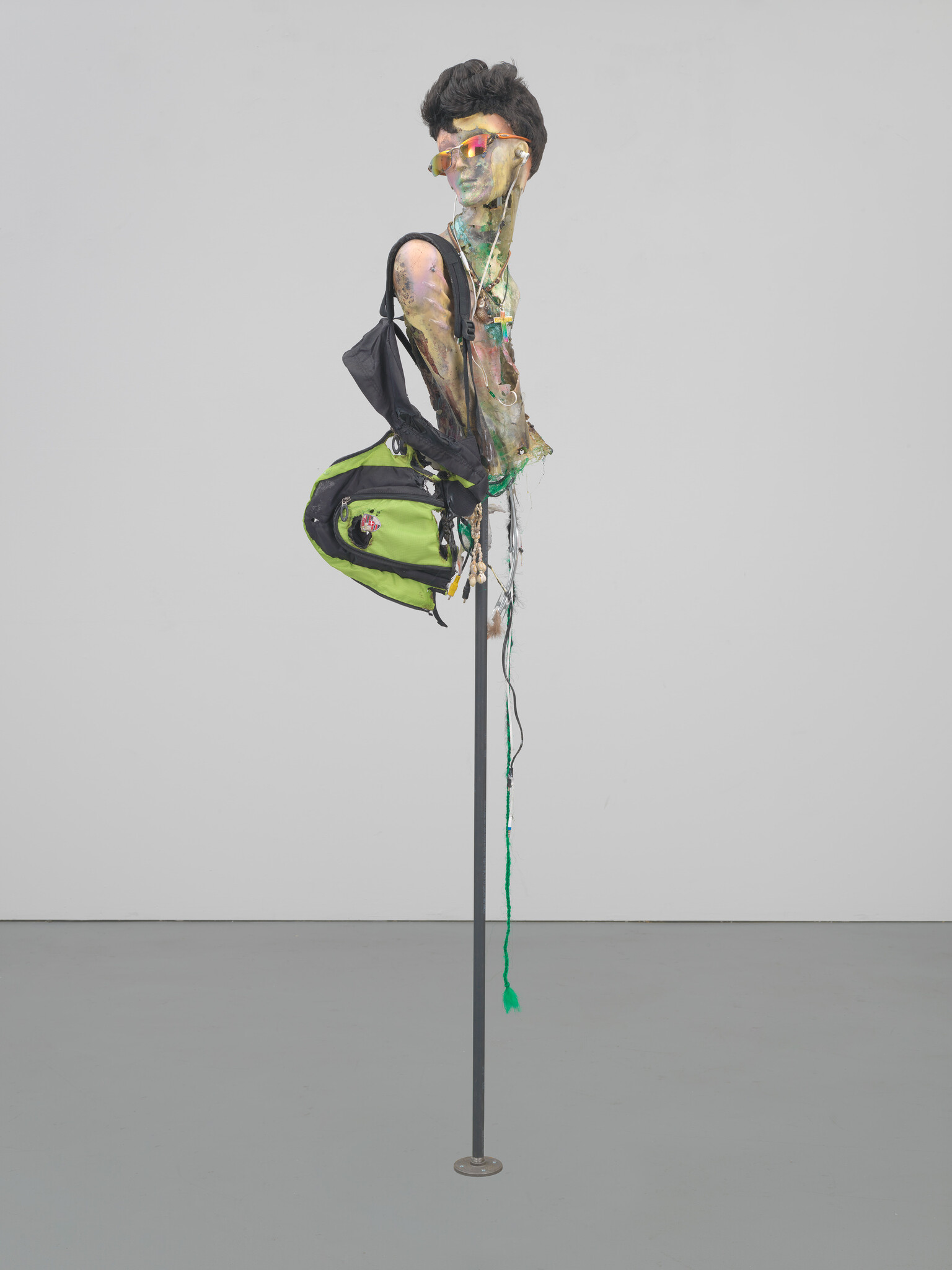A painted mannequin bust wearing sunglasses and a green backpack mounted on a tall metal pole.