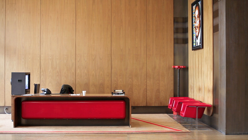 Reception desk with a red bench and three red chairs against a wood-paneled wall.