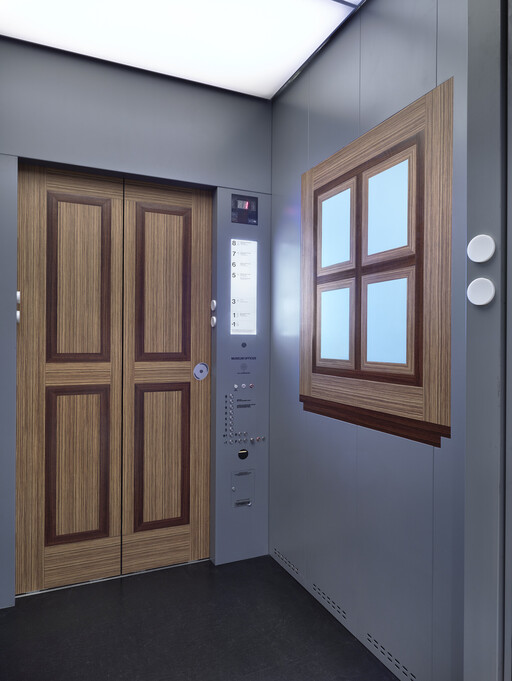 Elevator interior with wood-paneled doors, control panel, and a decorative window-like panel.
