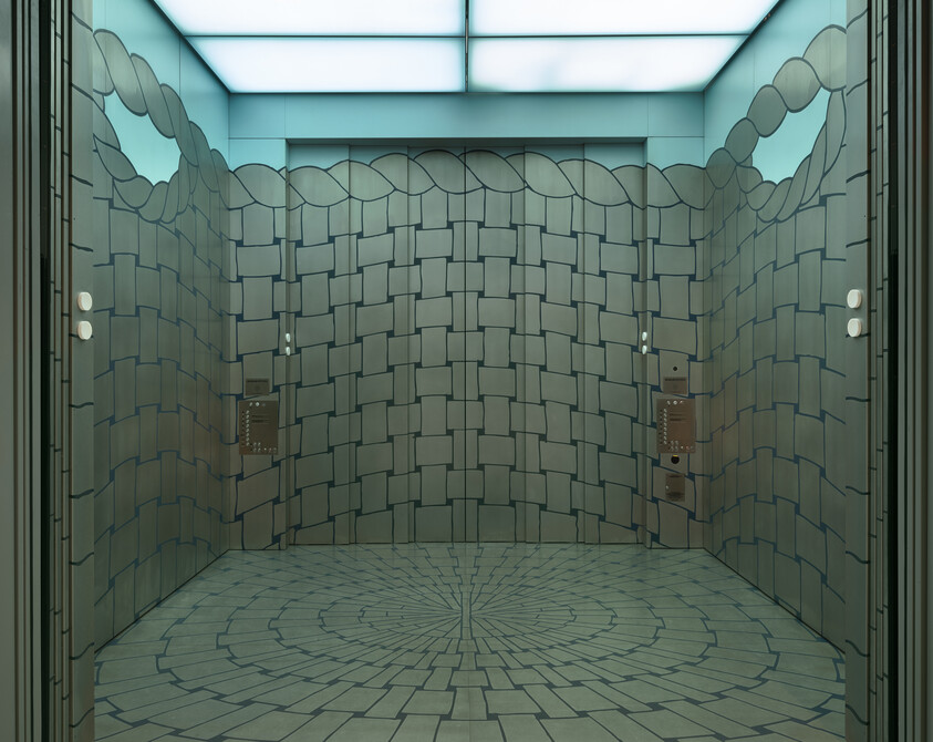 A 3D-rendered image of a room with stylized, uneven stone walls and a patterned floor that converges towards the center. The room has a skylight providing natural light, and there are lockers on one wall with a control panel beside them. The ceiling features a decorative, wave-like border.