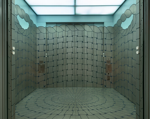 Elevator interior with woven tile walls and circular patterned floor under teal lighting.