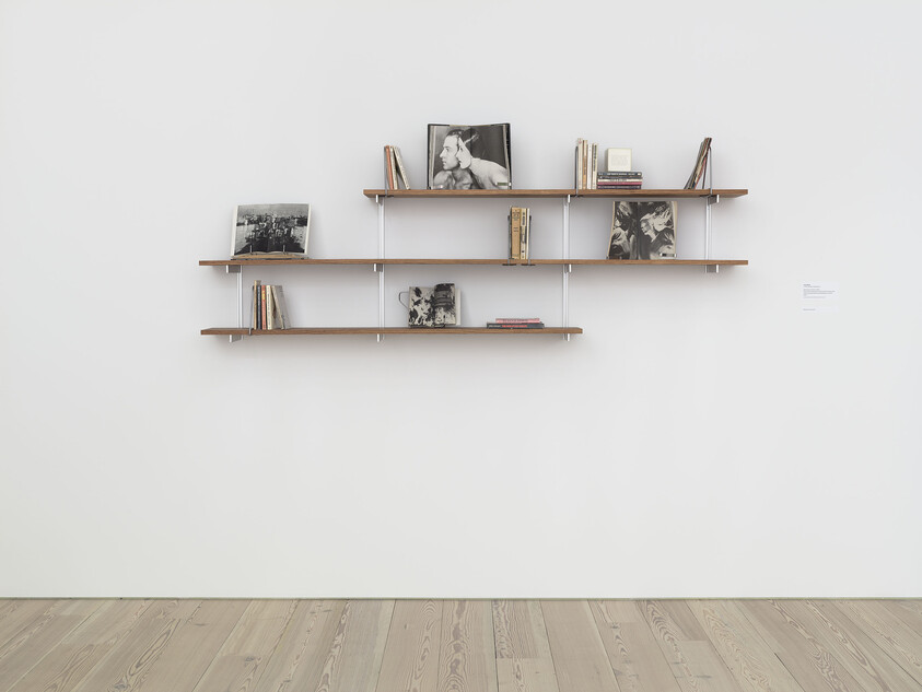 Wall-mounted wooden shelves displaying a few books and black-and-white photographs in a minimalist room.