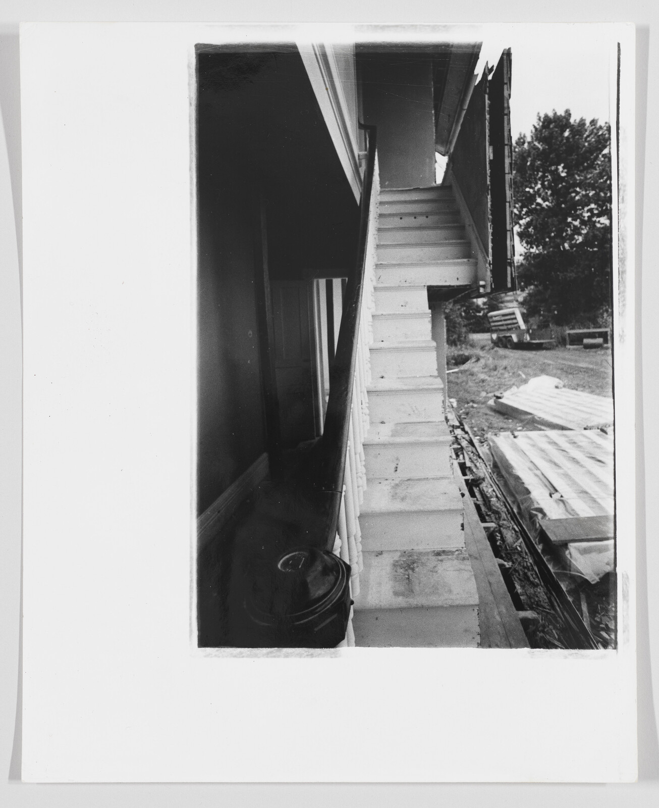 Narrow white porch staircase with worn steps beside scattered construction debris and metal sheets.