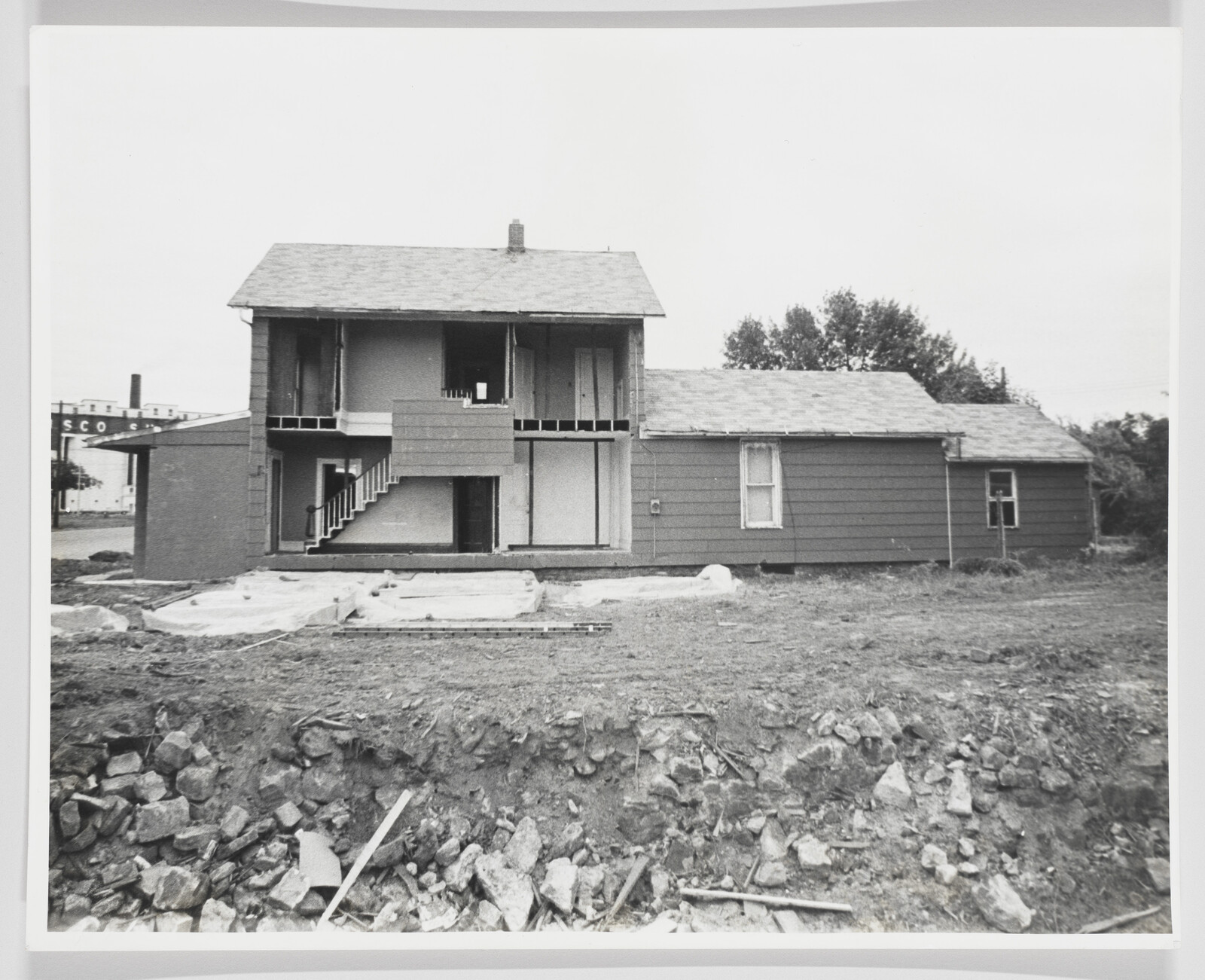 A partially demolished two-story house with exposed interior rooms and rubble in the foreground.